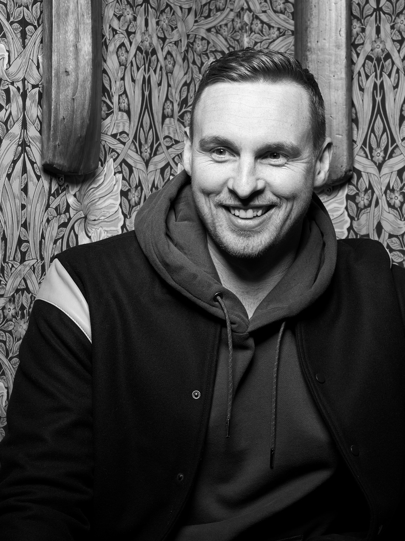 David Stockdale smiling and leaning on a bench with old cricket bats mounted on the wall behind